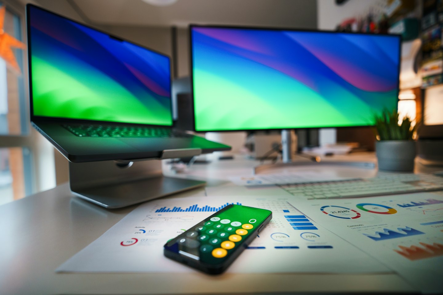 Desk with laptop, monitor, and papers with charts.